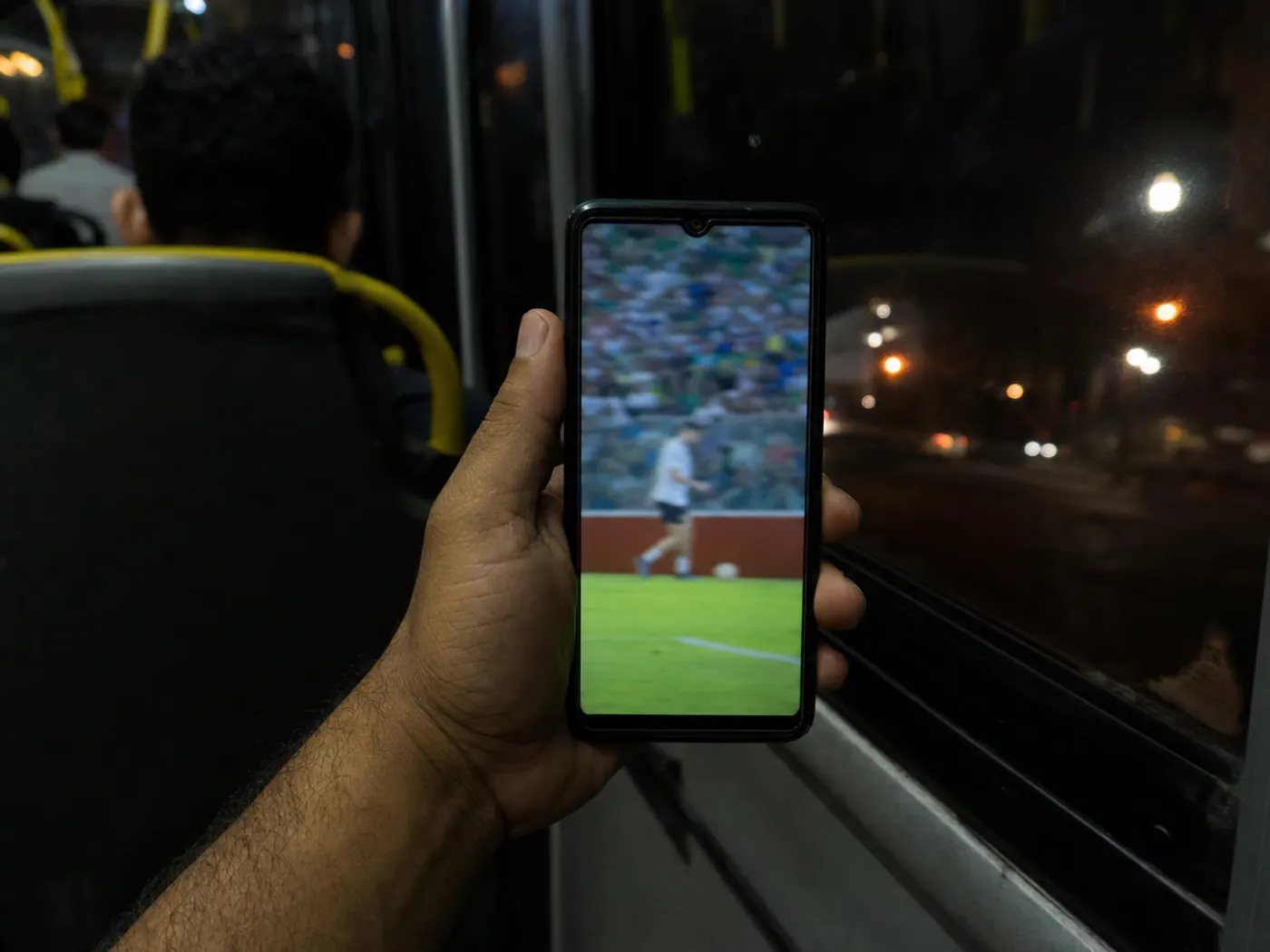 Mão segurando o celular firme, tela ligada com conteúdo, dia de semana qualquer